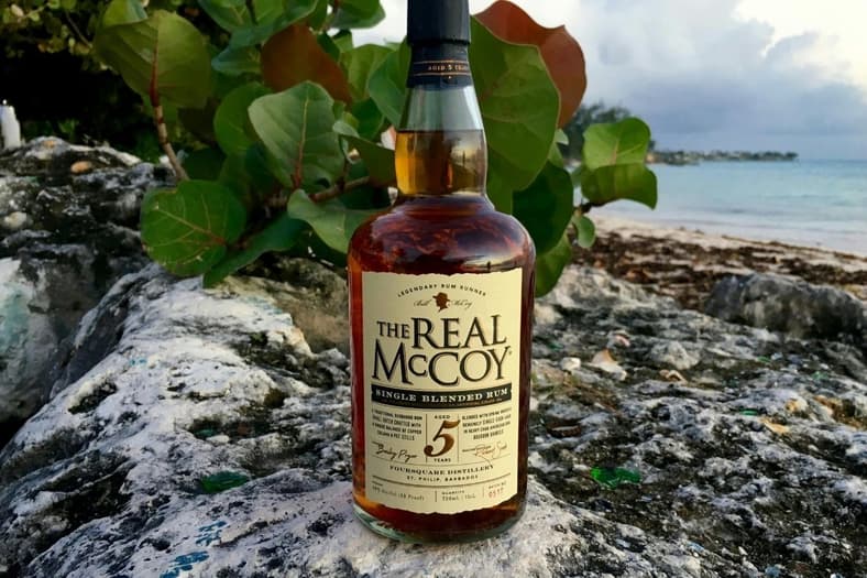 A bottle of rum positioned on a rock near water.
